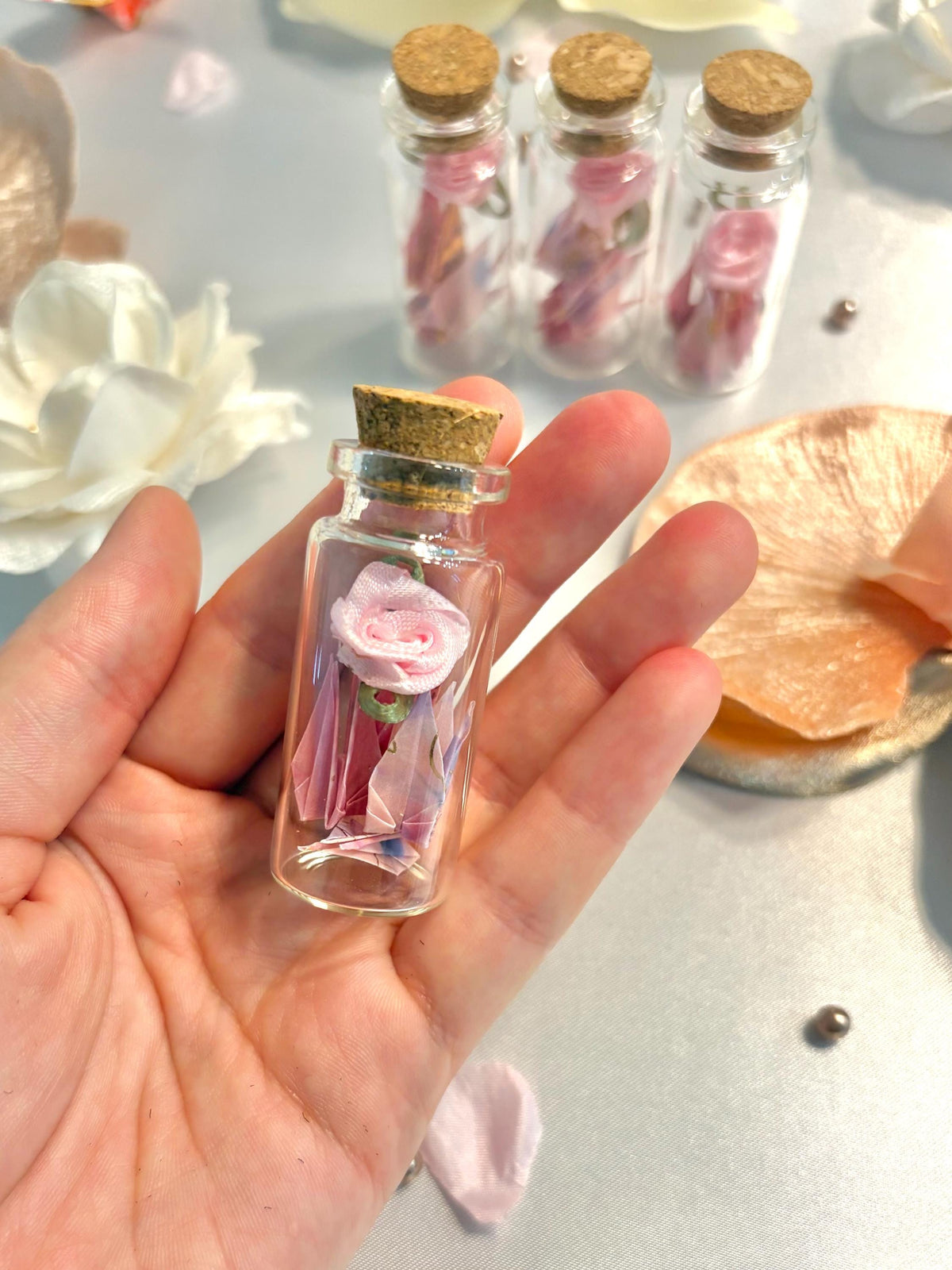 Mini origami cranes and a ribbon rose in a corked glass bottle